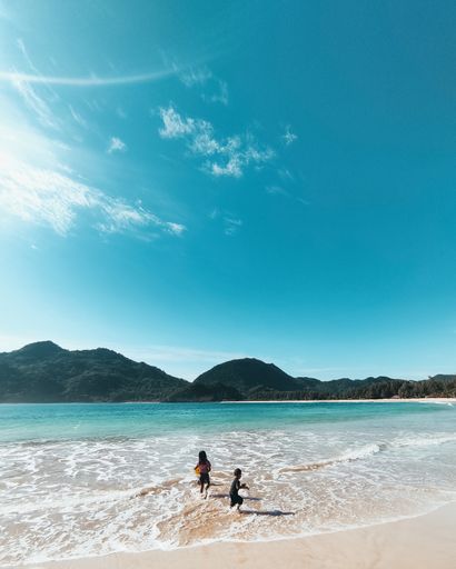 A beautiful landscape view of two kids playing in water beach with mountains with a sunny blue sky