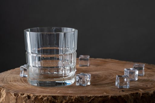 A closeup shot of an empty clear glass with ice cubes on a wooden surface