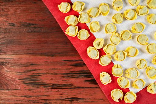  Italian  tortellini on white cloth, uncooked stuffed pasta on red wooden table