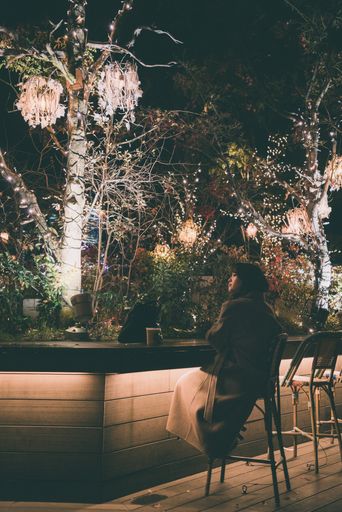 A young woman drinking coffee with illuminated trees for Christmas in the background in Tokyo