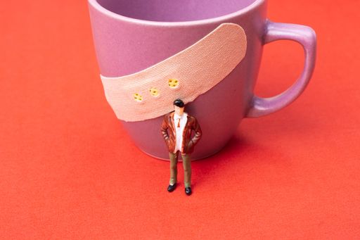 A closeup shot of a small plastic toy person standing in front of a purple cup with bandaid on it on a red surface