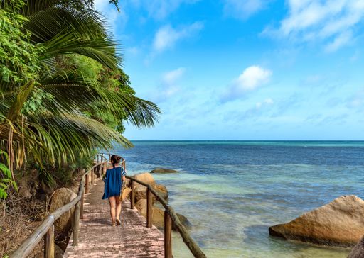 A woman walking on a wooden walkway over the sea in Praslin, Seychelles