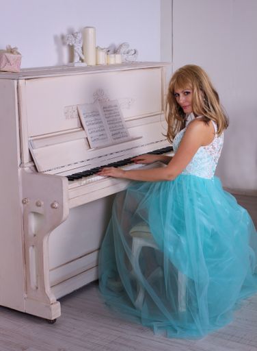 A beautiful shot of a Caucasian woman in a blue dress playing piano