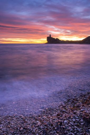 A panoramic view of a smooth sea hitting the rocky shore during sunset
