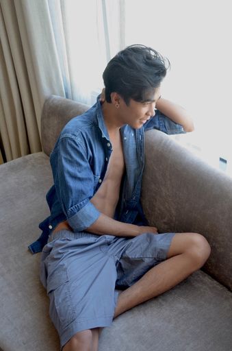 A vertical shot of a male sitting on a couch near the white curtains