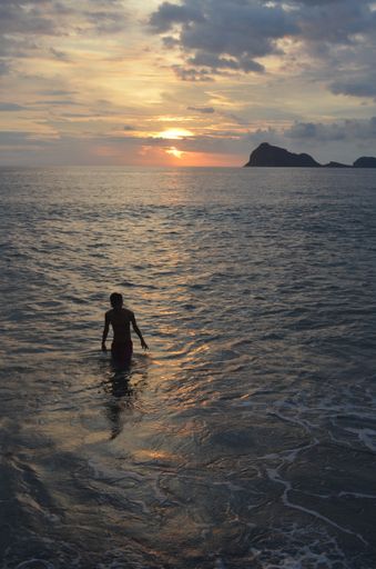 A vertical shot of a male walking in the water under a cloudy sky