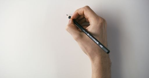 A hand of a man holding a pencil over white paper preparing to draw something