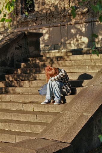 A vertical shot of a teenage girl sitting on the stairs on a sunny day portraying sadness and depression