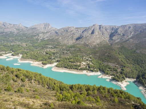 The Embalse de Guadalest surrounded by hills covered in greenery under the sunlight in Spain