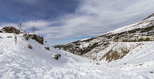 A low angle shot of snowy mountains and a rural area on the hill on a cloudy day