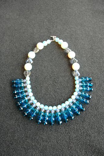A vertical shot of a necklace made of white and blue beads on a gray surface