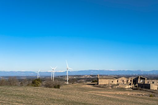 A field with white wind generators and brick buildings under the blue sky
