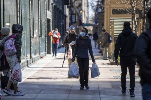 woman wearing a mask and gloves are carrying groceries after shopping for essentials during the covid-19 pandemic in Chicago downtown area. many are a