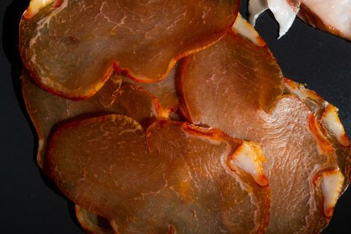 A closeup shot of thin-sliced raw pork meat on a black surface