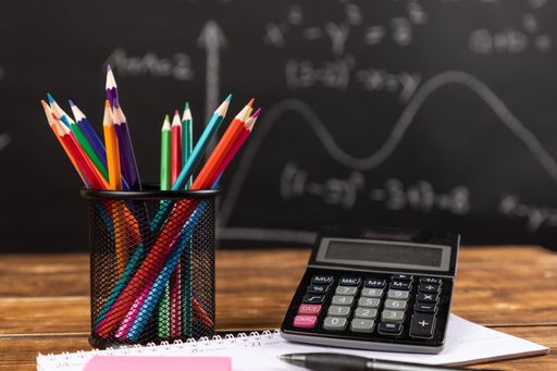 A stack of colored pencils with calculator and chalkboard