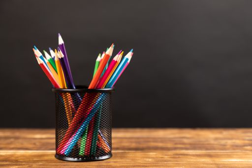A stack of colored pencils on wooden background with chalkboard school