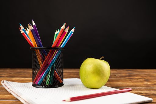 A stack of colored pencils with green apple on a black background