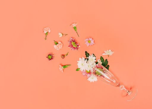 A creative minimal flat layout with various flowers and champagne glass on Paradise Pink background