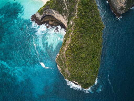 An aerial shot of the cliffs covered in greenery surrounded by the sea under the sunlight - perfect for backgrounds