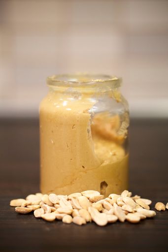 A vertical closeup of a homemade peanut butter, and peanuts on a wooden table