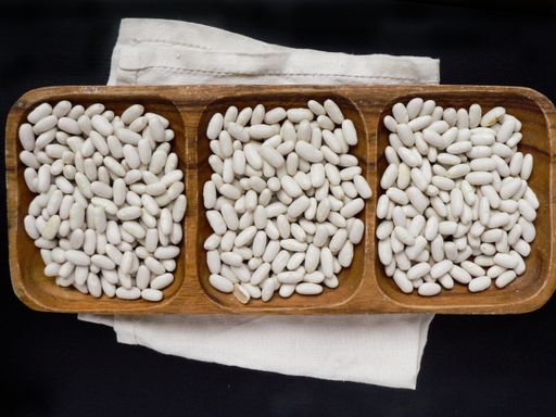 A top view of white raw beans in a wooden platter on a white napkin and black wooden table