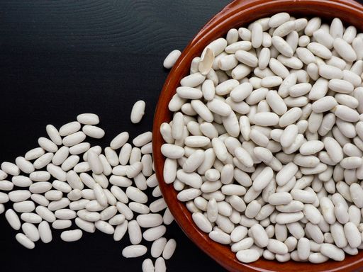 A top view of raw white beans in a clay bowl on a black wooden table
