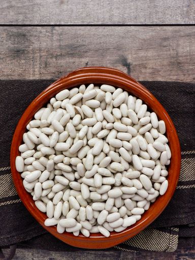 A top view of raw white beans in a clay bowl on a wooden table