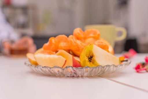 Slices of fresh apples and tangerines lie on a glass dish. Sweet fruit salad. In the background are cups of hot drinks.