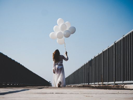 A beautiful female with white balloons on a bridge under the clear sky