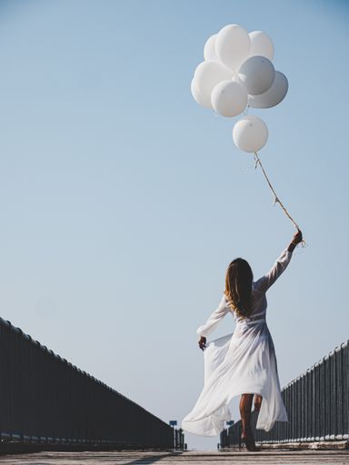A beautiful female with white balloons on a bridge under the clear sky