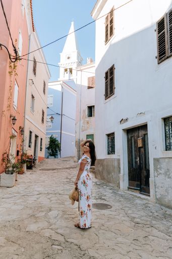 A vertical rear view of a young woman smiling and looking back at the camera in the idyllic old town in Vrsar, Croatia.