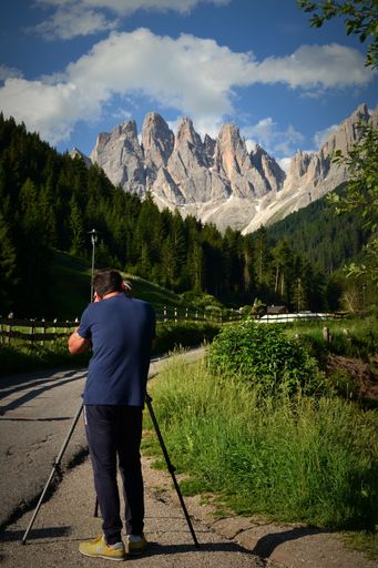 A vertical shot of a photographer taking a photo of a mountain view from the forest