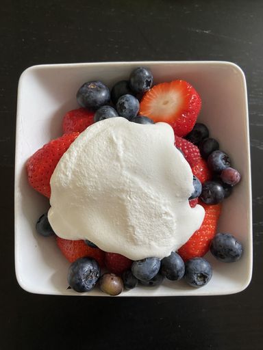 A closeup shot of yogurt with blueberries and strawberries in a white plate on black background