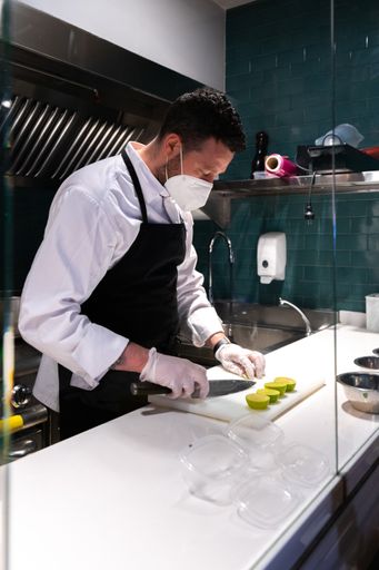 A vertical shot of a chef wearing a face mask holding a knife on a chopping board