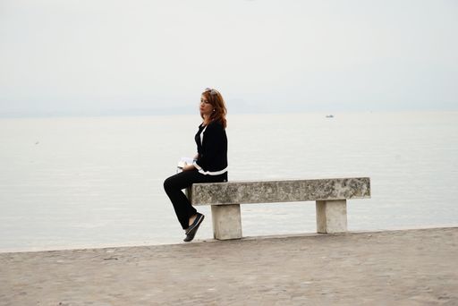 A side view of a German woman sitting on the edge of a stone bench on the beach