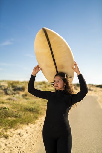 A vertical shot of an attractive female carrying a surfboard above her head in the middle of the road in Spain