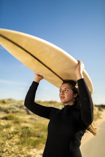 A vertical shot of an attractive female carrying a surfboard above her head in the middle of the road in Spain