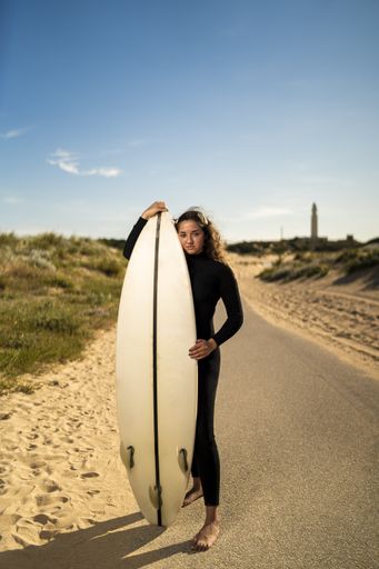 A vertical shot of an attractive female holding a surfboard in the middle of the road in Spain