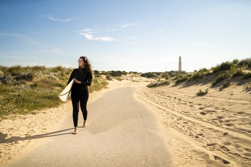 A shallow focus shot of an attractive female carrying a surfboard while walking in the middle of the road in Spain