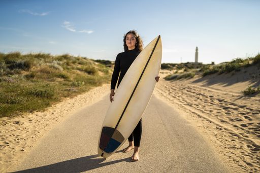A shallow focus shot of an attractive female holding a surfboard in the middle of the road in Spain