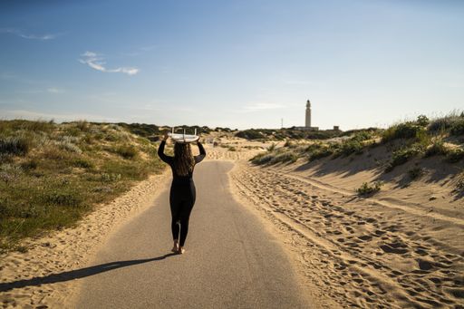 An attractive female carrying a surfboard above her head while walking in the middle of the road in Spain
