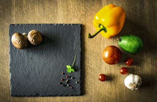 A vegetable composition with pepper, tomato, avocado, garlic and mushrooms on a black chopping board