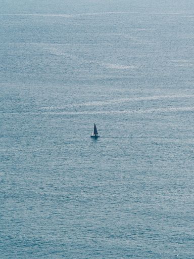 A vertical shot of a little sailboat in the middle of the blue sea