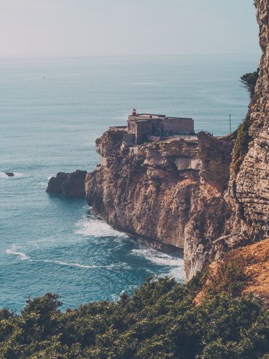 A vertical shot of a huge cliff with a building on it on the coastline
