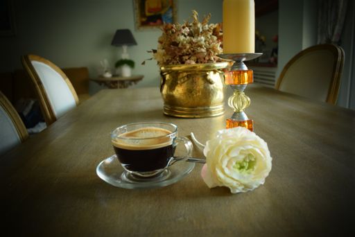 A closeup shot of a cup of dark coffee with a white flower, a candle and home decors on the table