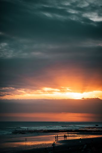 A vertical shot of silhouettes of people at the beach during the beautiful sunset