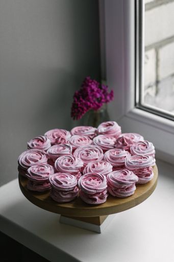 A vertical high angle shot of tasty pink desserts on a wooden plate near the window