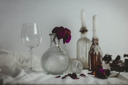 Two candles on the bottles next to a vase with a flower inside and a glass