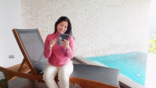 Asian woman relaxing on a pool bed and using digital tablet near the private pool during her morning vacation.