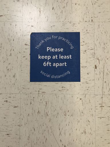 A blue sign asking people to keep a minimum distance of each other on the wall